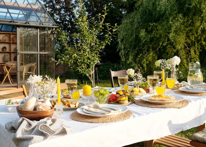 Gedeckter Gartentisch mit weißem Tuch, gelben Kerzen und einem Krug Limonade