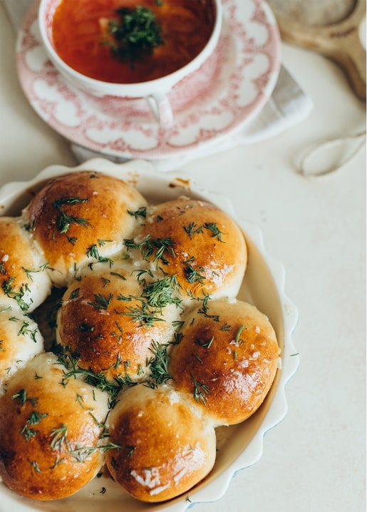 Goldene Knoblauchbrötchen neben einer Schale roter Suppe in einer Vintage-Blumentasse