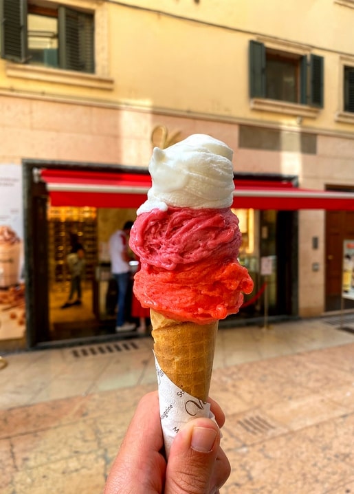 Eiswaffel mit Beerensorbet vor einer Straße mit rotem Sonnenschirm in Italien
