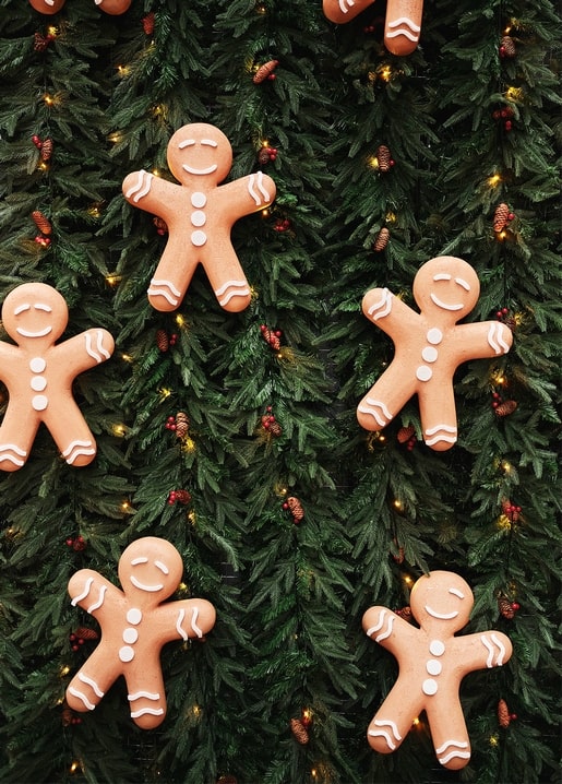 Smiling gingerbread men decorating fir branches with fairy lights and pinecones