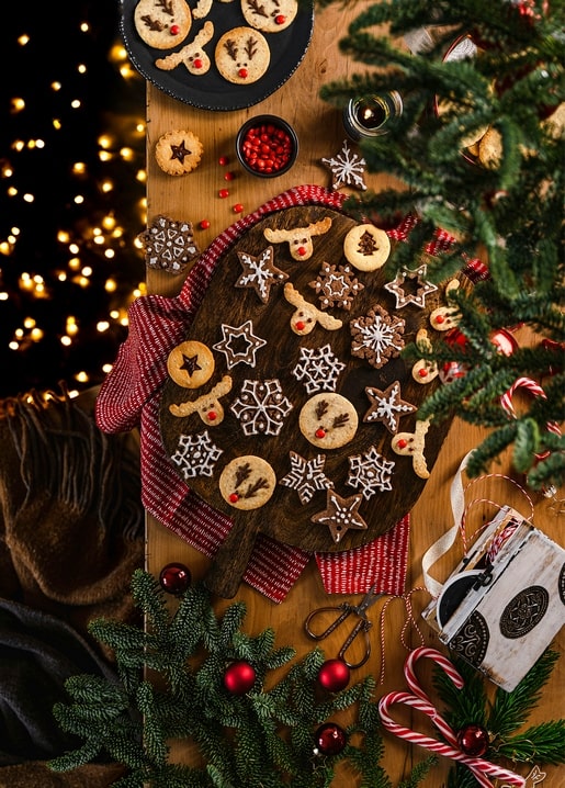 Iced star and snowflake cookies with gingerbread reindeer on a wooden board with pine branches
