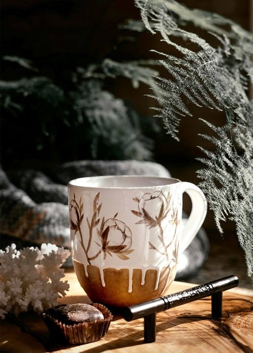 Gold-dipped mug with painted flowers beside frosted fern branches and white coral