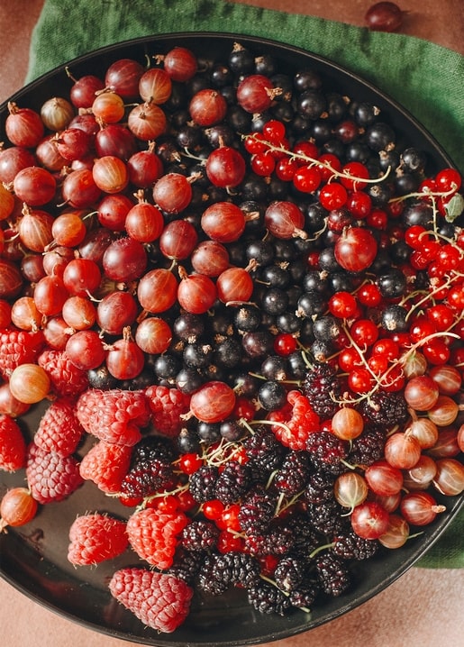 Stachelbeeren, schwarze und rote Johannisbeeren, Himbeeren und Brombeeren auf einem schwarzen Teller