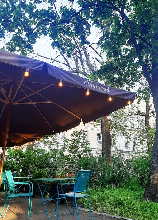 Turquoise café chairs under a string-lit umbrella on the Gorky terrace, Kyiv evening