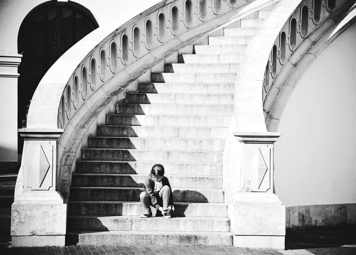 Person tying shoelaces on the steps of a monumental curved staircase, black-and-white photo