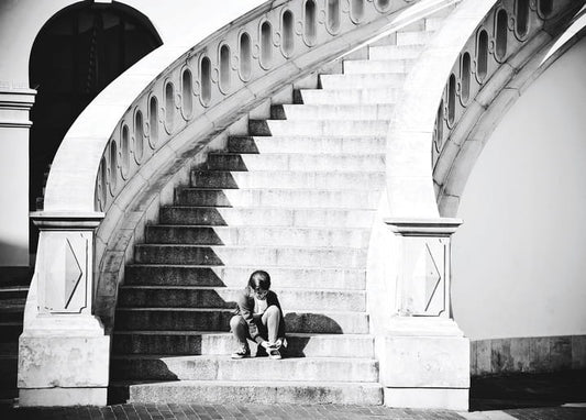 Person tying shoelaces on the steps of a monumental curved staircase, black-and-white photo