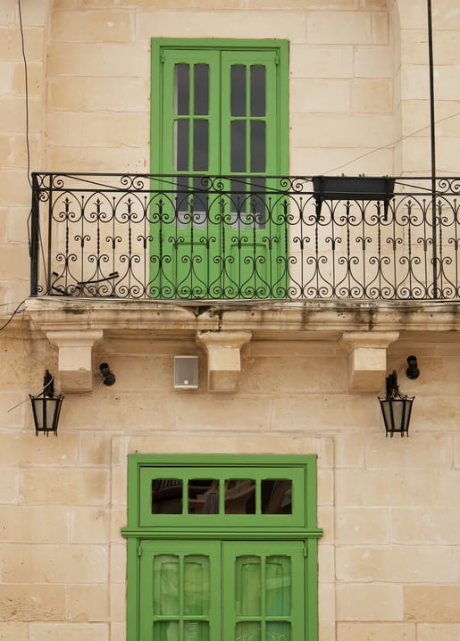 Green balcony doors with wrought-iron railing on a stone building facade