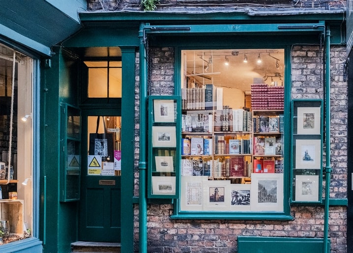 Green-painted vintage bookshop storefront with framed prints, glowing at dusk