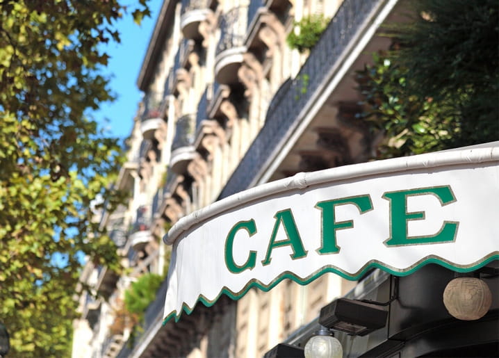 Green-and-white striped café awning with 'CAFE' lettering below Haussmann-style Paris balconies