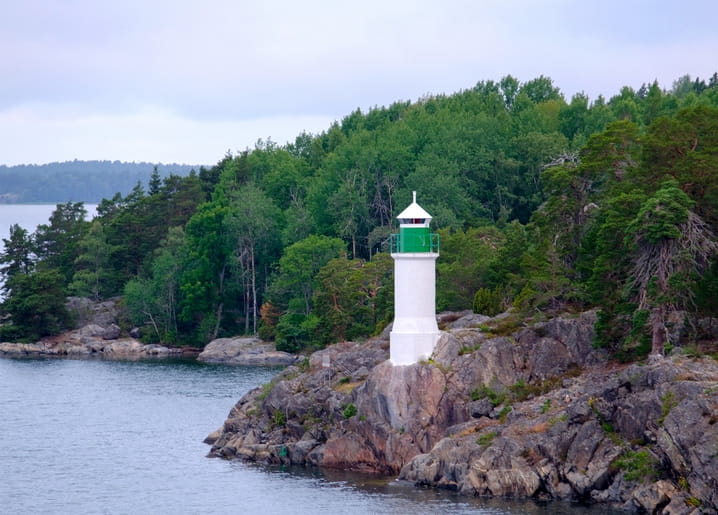 Grün-weißer Leuchtturm auf Granitfelsen an bewaldeter Sommerküste