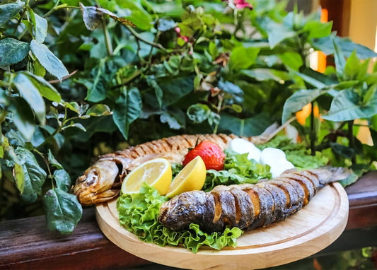 Zwei gegrillte Fische mit Zitrone, Tomate und saurer Sahne auf einem Holzbrett