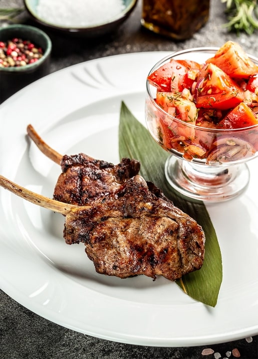 Gegrillte Lammkoteletts mit Tomaten-Zwiebel-Salat auf weißem Teller