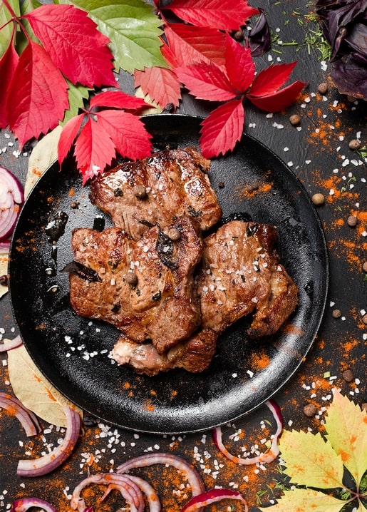 Gegrilltes Fleisch auf schwarzem Teller umgeben von rotem Herbstlaub