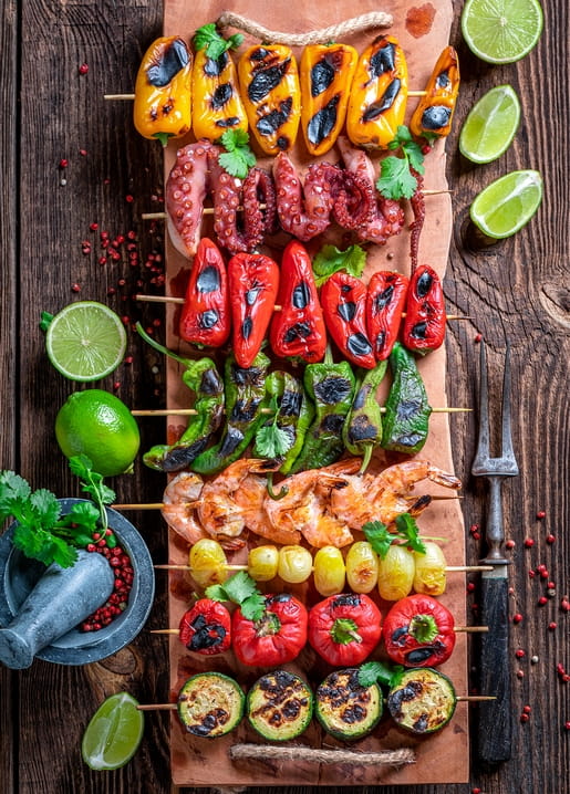Spieße mit Paprika, Oktopus und Garnelen auf Holzbrett mit Limetten