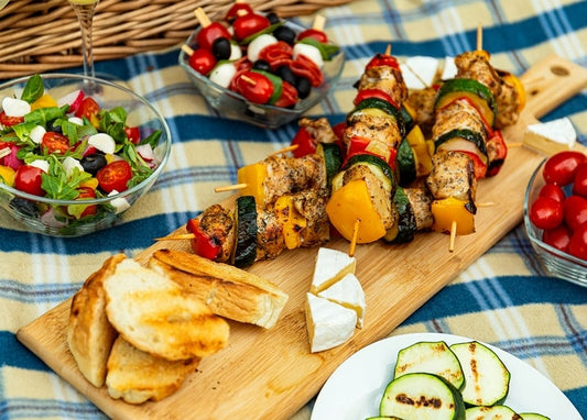 Grilled skewers, salad and bread arranged on a plaid picnic blanket