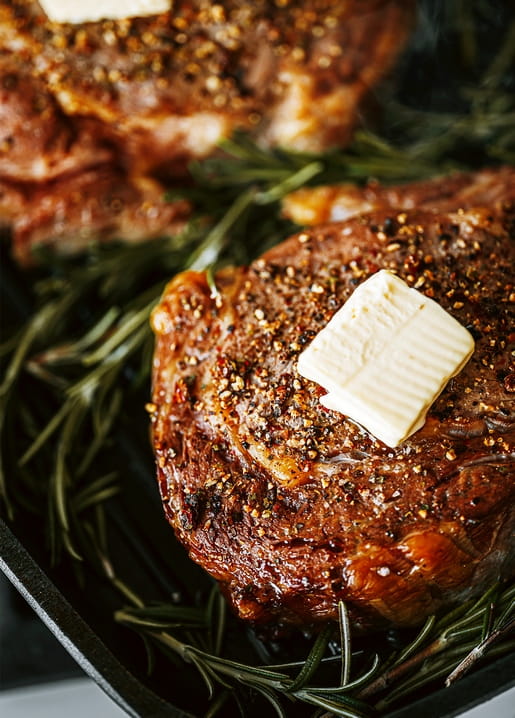 Grilled steak with melting butter and cracked pepper on a bed of fresh rosemary sprigs