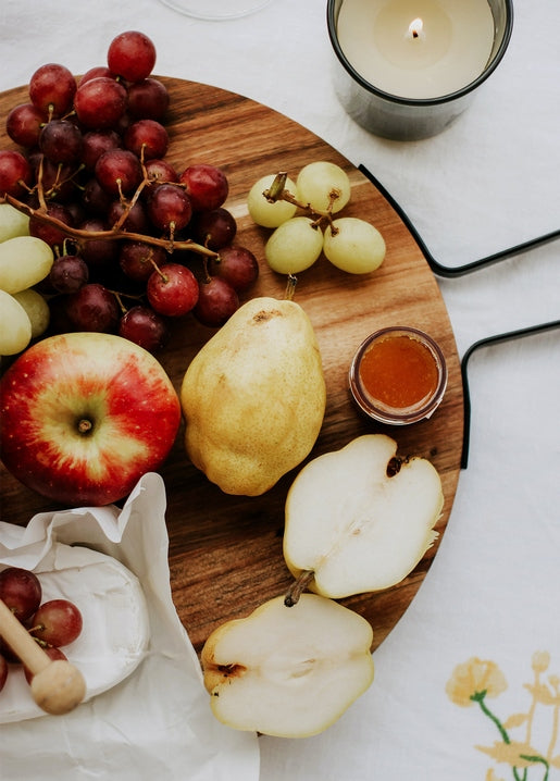 Wooden board with grapes, apple, pears, honey, cheese, and a lit candle