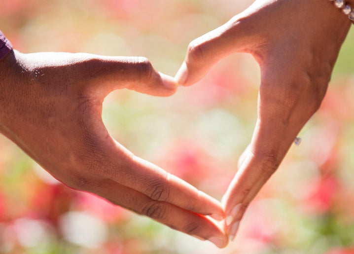 Two hands forming a heart shape against blurred pink summer flowers