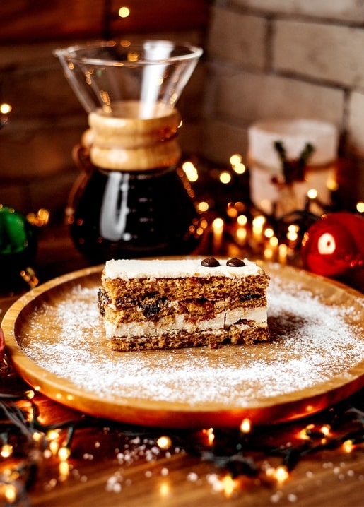 Slice of honey layer cake beside a glass pour-over coffee maker and fairy lights