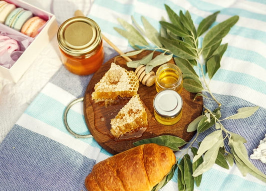 Honigglas, Honigwaben und Croissant auf gestreifter Picknickdecke mit Olivenzweigen