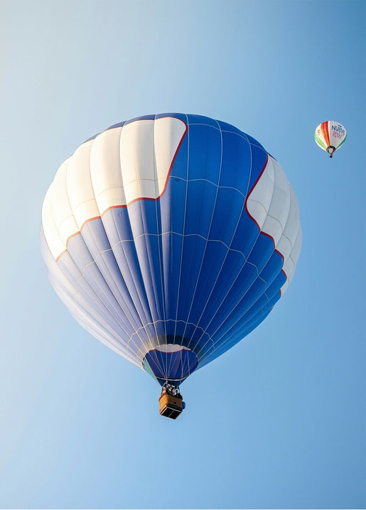 Striped blue-and-white hot air balloon rising against a clear blue sky with a smaller balloon in the distance