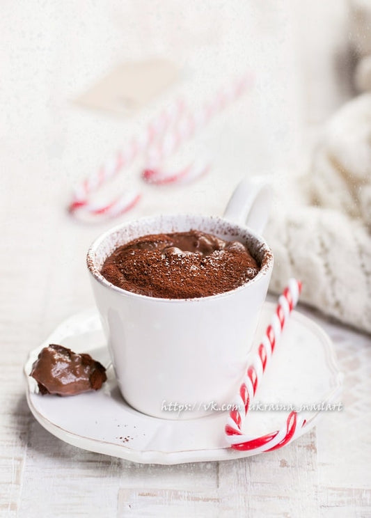 Tasse heiße Schokolade mit Kakaopulver, Zuckerstangen und einer Strickdecke im Hintergrund