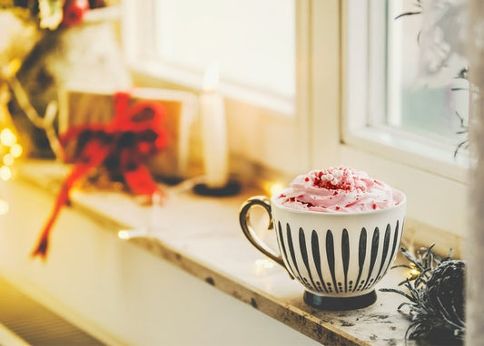 Cup of hot chocolate with pink whipped cream beside a wrapped gift