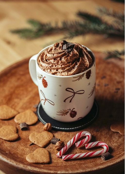 Mug of hot cocoa with whipped cream, gingerbread hearts and candy canes on a wooden table