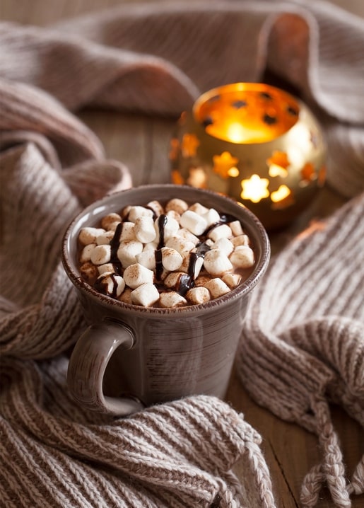Becher heiße Schokolade mit Marshmallows neben Sternlaterne und Schal