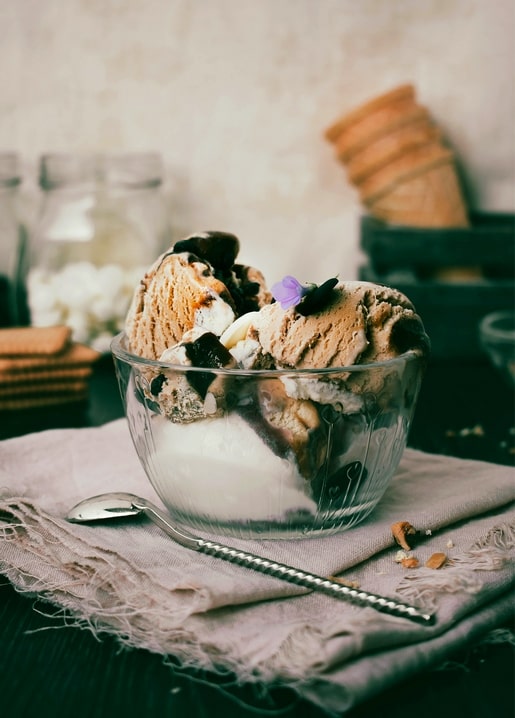 Eisdessert in einer Glasschale mit Löffel, Marshmallows und einer violetten Blüte