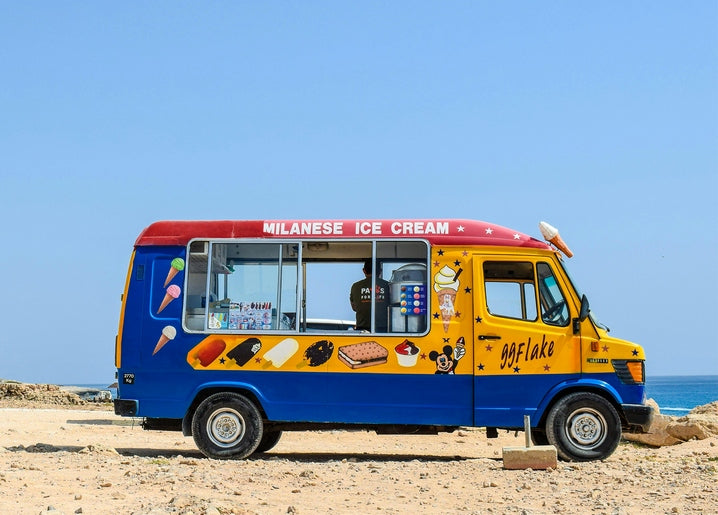 Blue and yellow ice cream van parked on a sunny beach by the sea