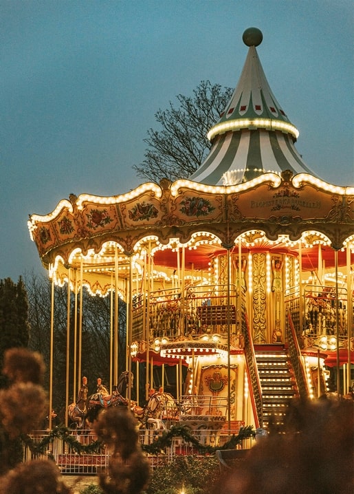 Illuminated double-decker carousel with carved horses at a winter fair at dusk