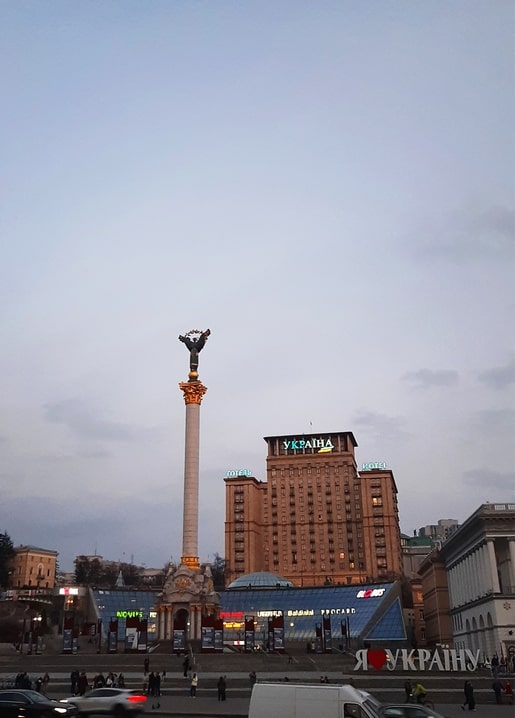 Independence Monument column glowing at dusk with Hotel Ukraina in the background