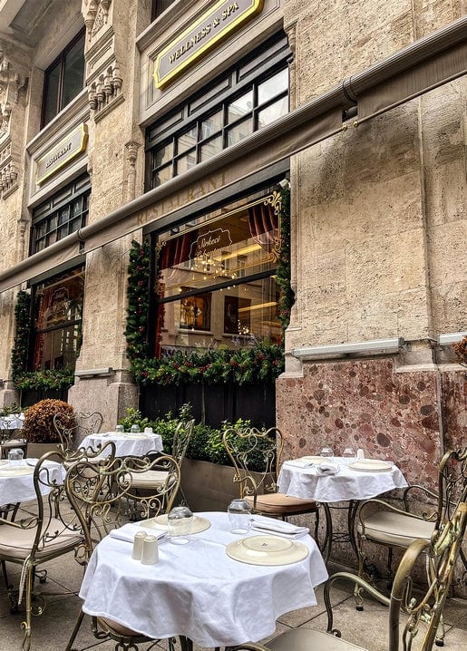 Empty white-clothed café tables on a stone terrace beneath garland-wrapped windows in Italy