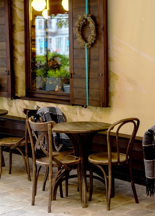 Bentwood chairs and plaid blankets outside a café with a wreath-hung window in Ivano-Frankivsk