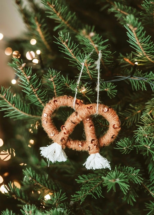 Handmade jute pretzel ornament with sequins and tassels on a Christmas tree branch