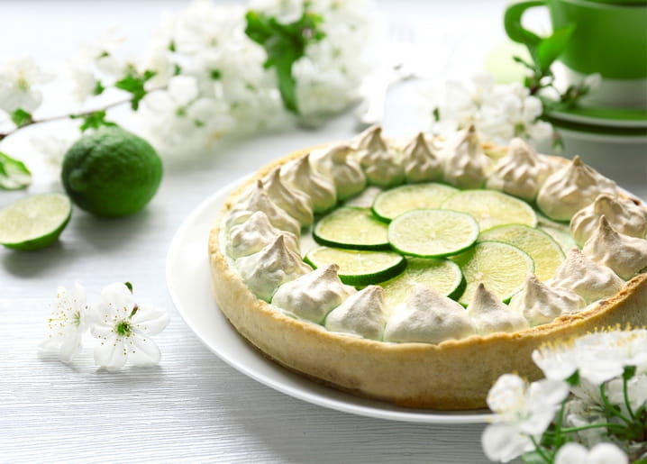 Key lime meringue pie with lime slices, white cherry blossom branches and a green teacup