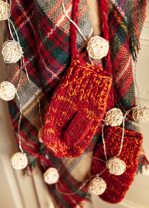 Red knit mittens and fairy lights against a plaid blanket