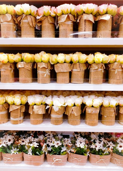 Rows of kraft-paper-wrapped roses on florist shelves above baskets of white daisies