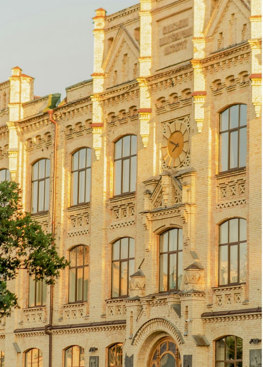 Golden-hour view of an ornate Kyiv building facade with carved cornices, arched windows and a clock.
