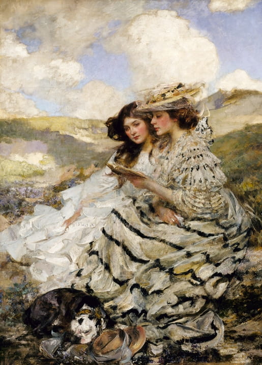 Two women in white dresses read a book together on a grassy sea dune, a spaniel resting beside them
