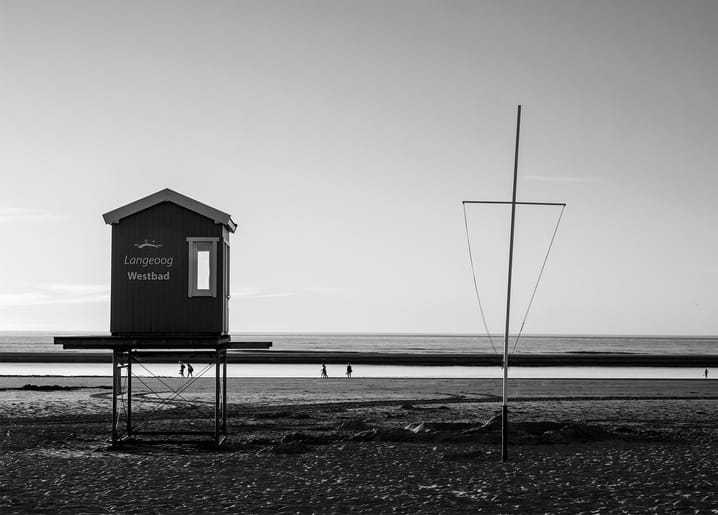 Black-and-white photo of the Langeoog Westbad beach hut on stilts with a wire sculpture