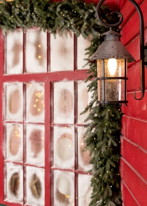Wrought-iron lantern glowing against a red wall beside a frosted multi-pane window