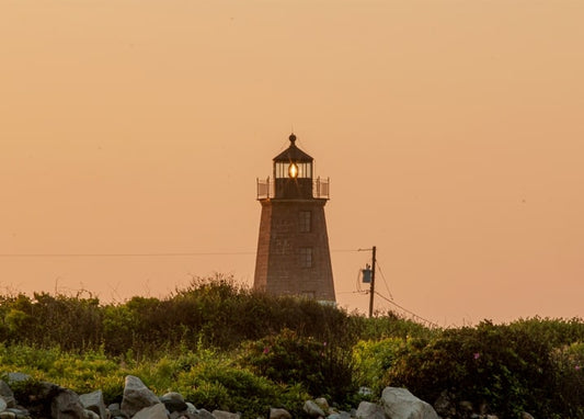 Steinleuchtturm leuchtet in der Dämmerung über einer felsigen Küste mit Rosenbüschen