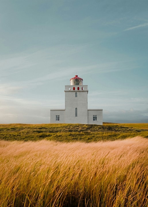 Weißer Leuchtturm mit rotem Laternenhaus auf einem Hügel über goldenem Herbstgras