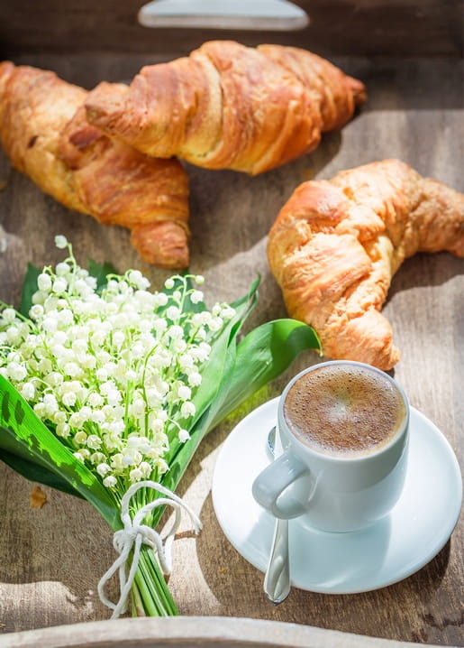 Lily of the valley tied with twine beside coffee and croissants on a wooden tray