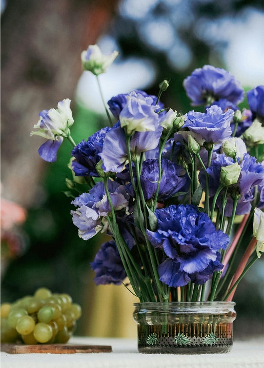 Blue and white lisianthus bouquet in a glass jar with green grapes beside it