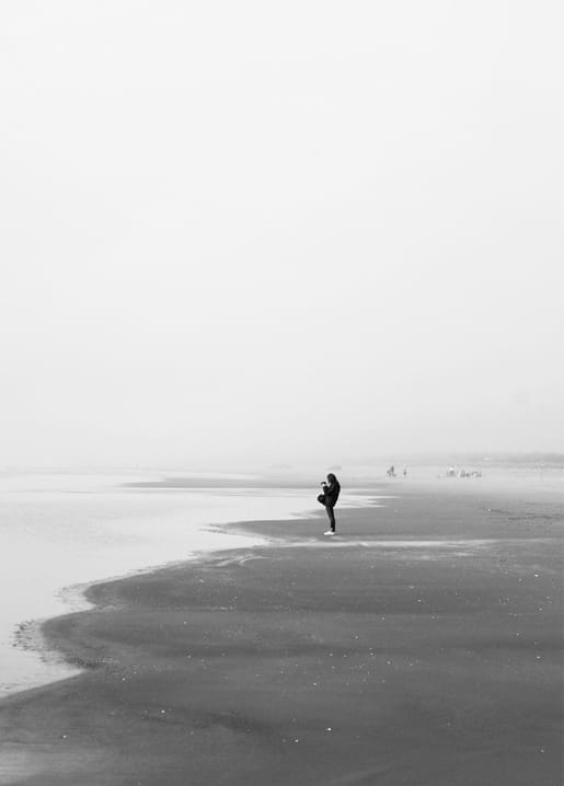 Black-and-white photo of a lone figure standing on a foggy, wide beach
