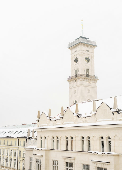Weißer Uhrturm des Lemberger Rathauses vor winterlichem Himmel über verschneiten Dächern