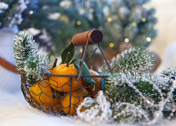 Mandarins in a wire basket among frosted pine branches and warm lights